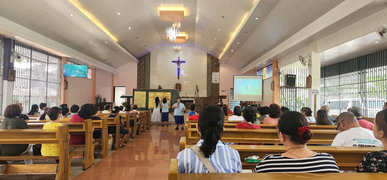 People in the pews of a church, facing a speaker and a projected slide at the front