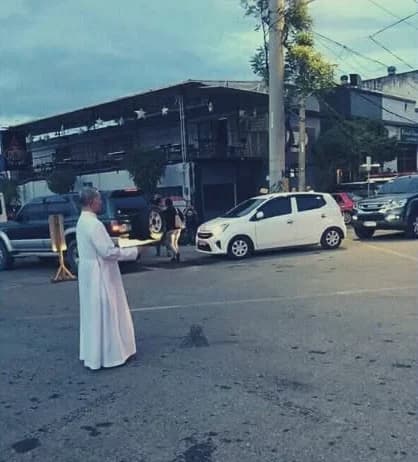 Msgr. Fred, in a white cassock, standing in the middle of a city street at dusk, directing the cars around him.