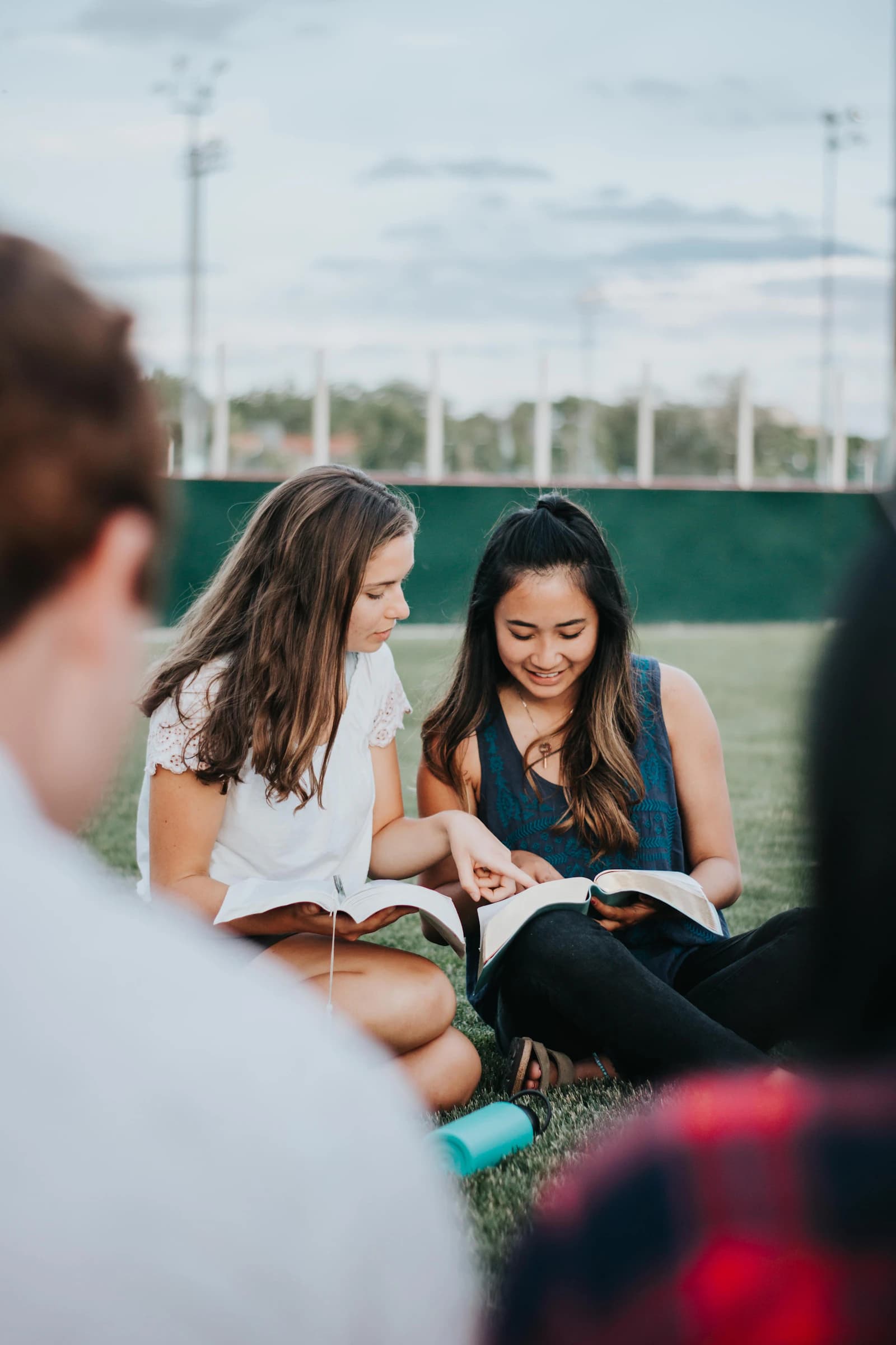 A group of people sitting on the ground, reading a book together.