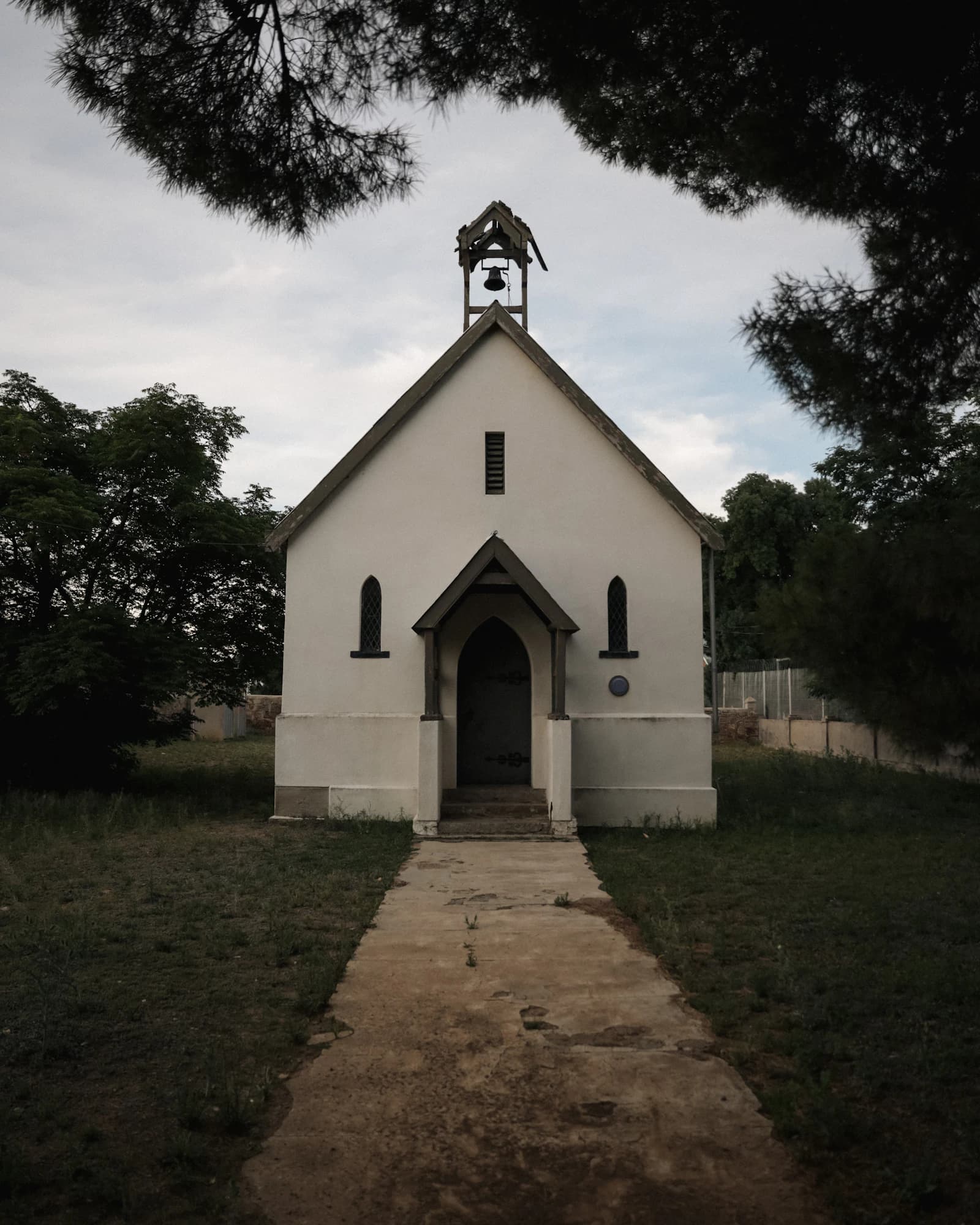 A small white chapel with a bell tower at the end of a garden path.